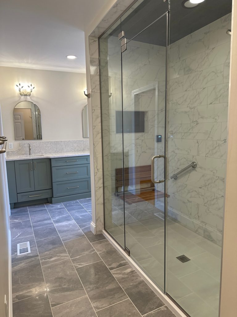 Marble shower with teak bench beside a green vanity