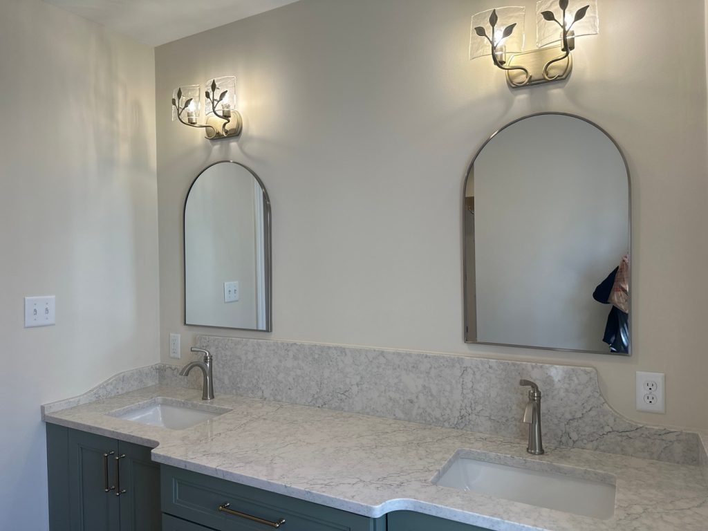 Double vanity with leaf sconces and arched mirrors
