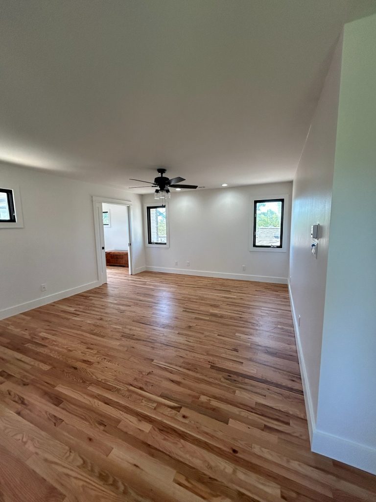 Empty living room with hickory floors and black windows