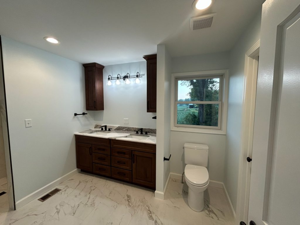 Bathroom with double vanity, toilet and rural view window