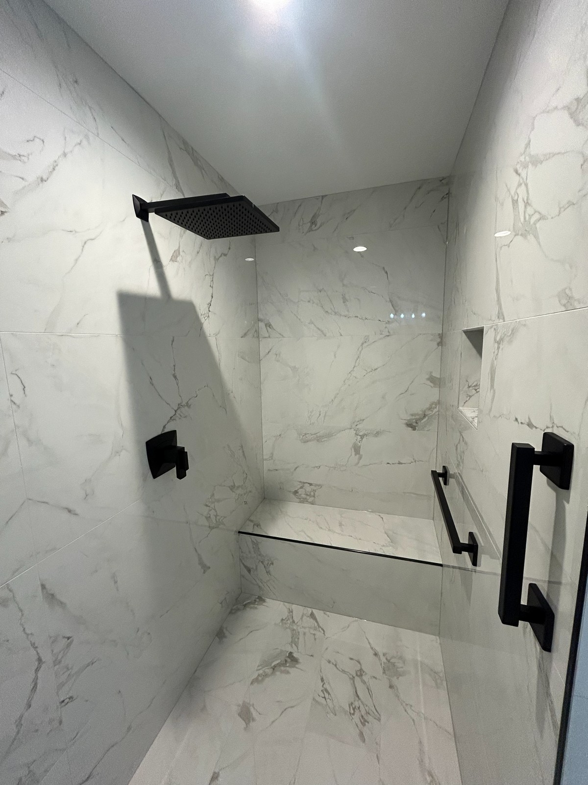 Marble-tiled shower with recessed niche and black fittings