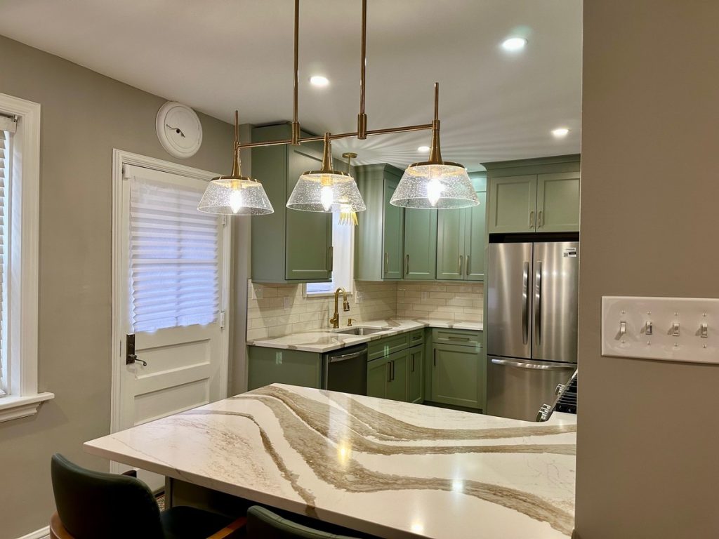 Sage green kitchen with brass pendants and quartz peninsula