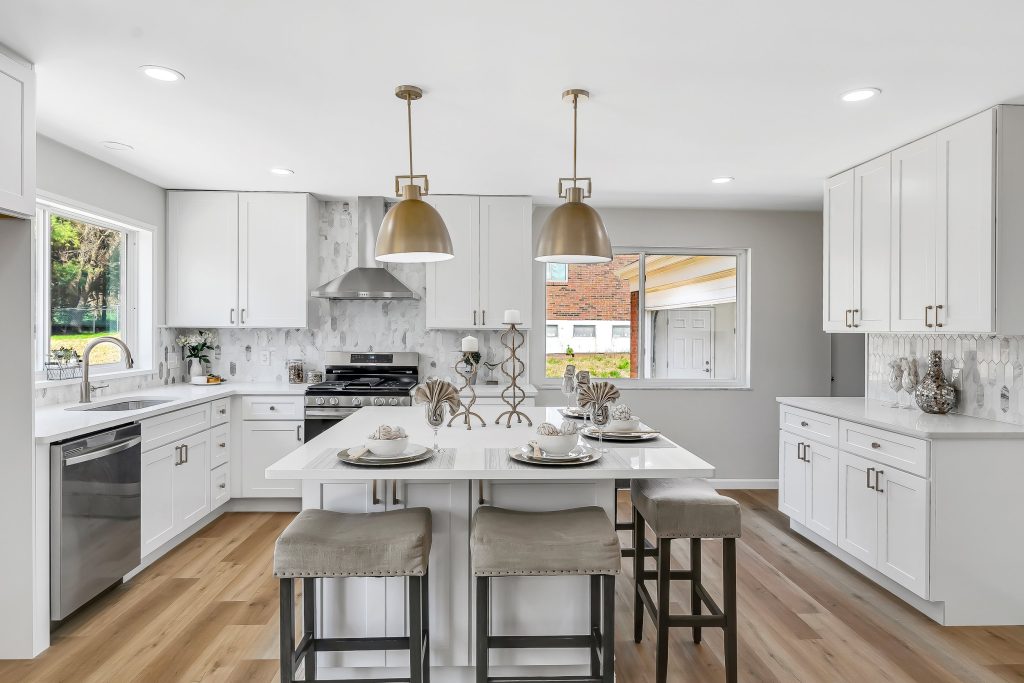 Kitchen with white cabinets, island stools and stainless dishwasher