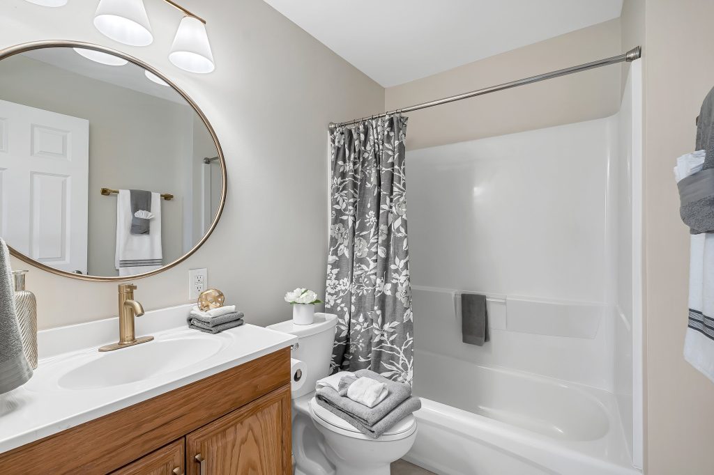 Bathroom with white vanity, round mirror and tub surround