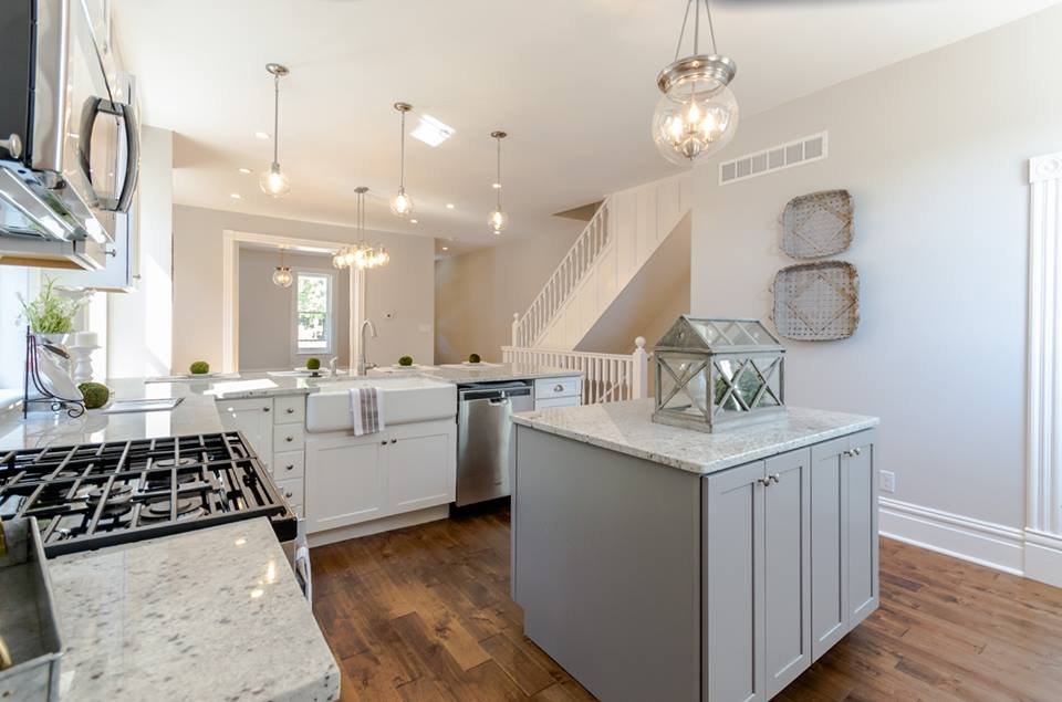Renovated kitchen with gray island, white cabinets and glass pendant lights