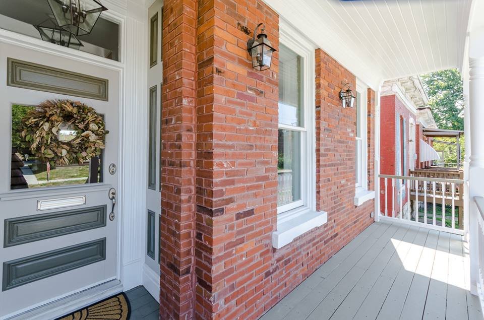 Covered front porch with exposed brick wall and wreathed front door