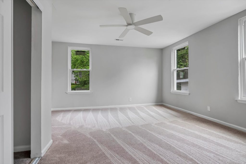 Empty carpeted bedroom with ceiling fan and two windows