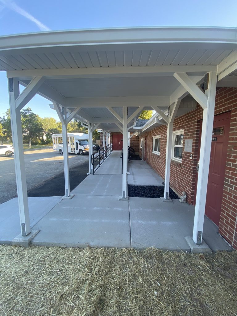 Covered walkway with white posts alongside the brick building