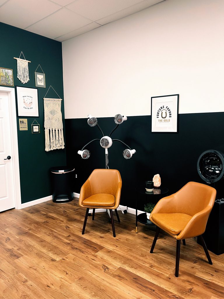 Salon waiting area with tan chairs and dark green wall