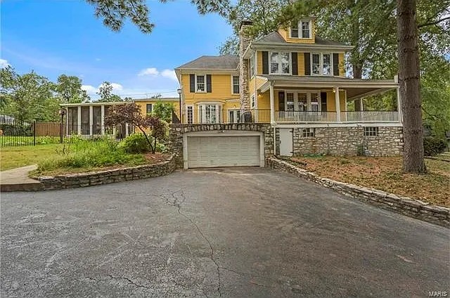 The original house from the driveway, with its stone retaining wall and yellow siding