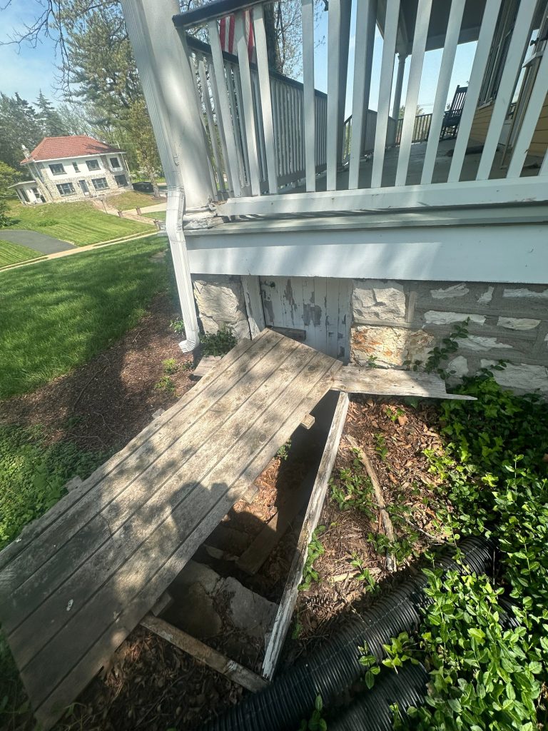 Deteriorated exterior wood steps beside the original stone wall