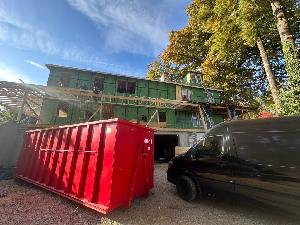 Dumpster in the driveway beside the house in its housewrap