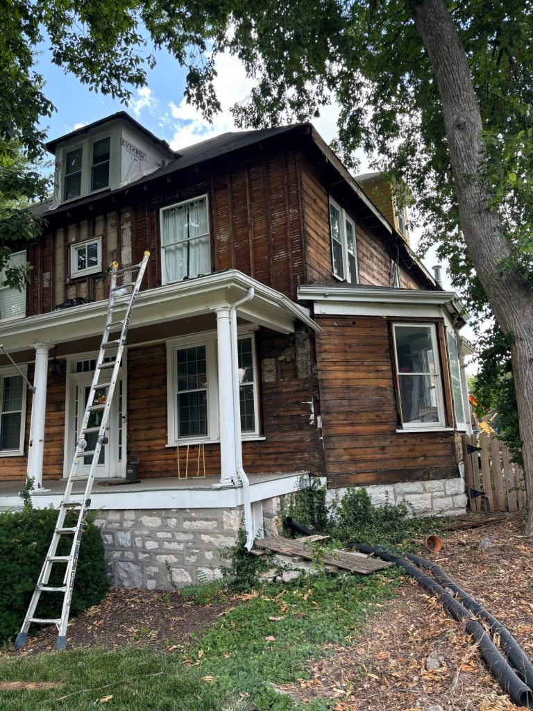 Original siding stripped back to bare wood, with the stone foundation exposed