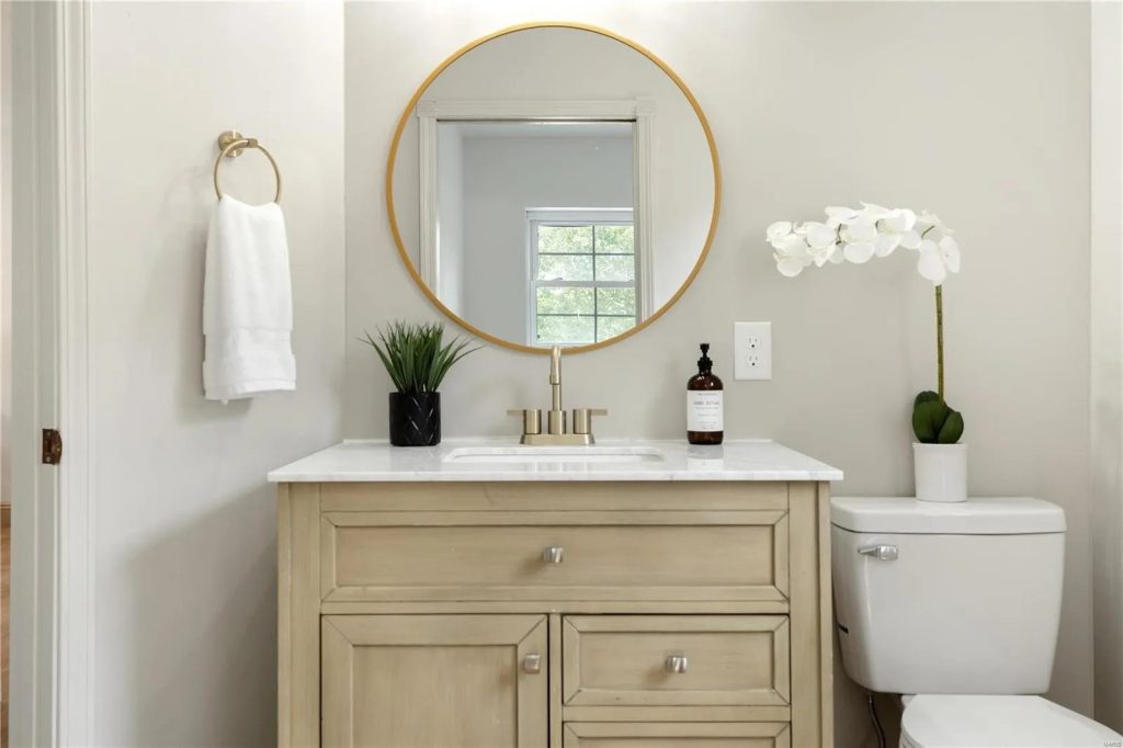 Powder room with wood vanity and round gold mirror
