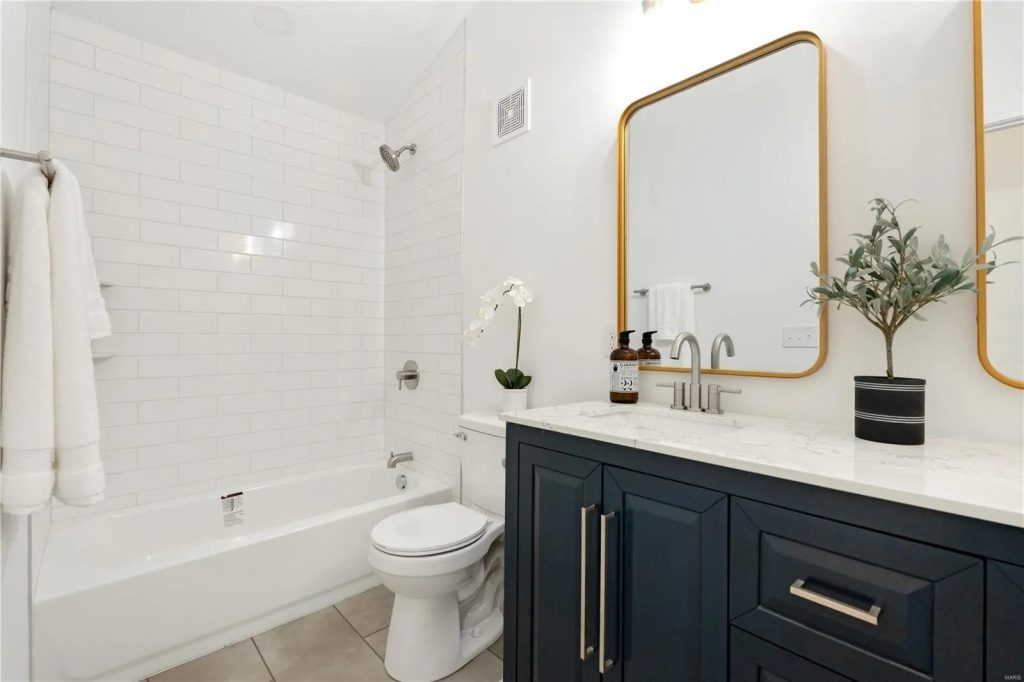 Bathroom with navy vanity, gold mirror and tiled tub