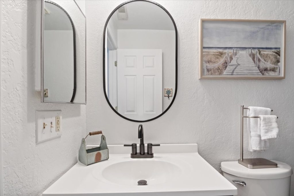 Bathroom vanity with oval mirror and coastal artwork